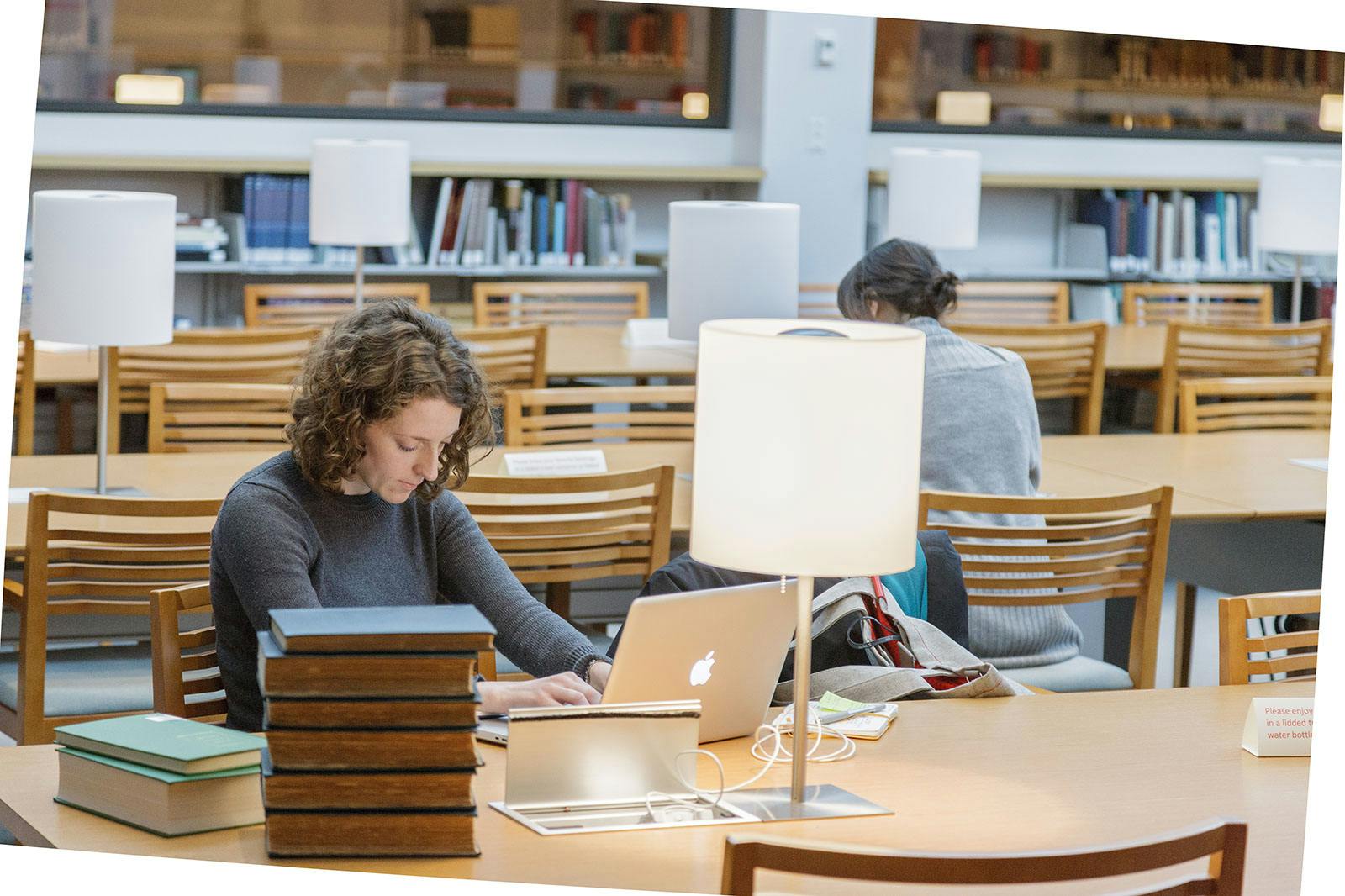 person working on laptop with stack of books at table in library