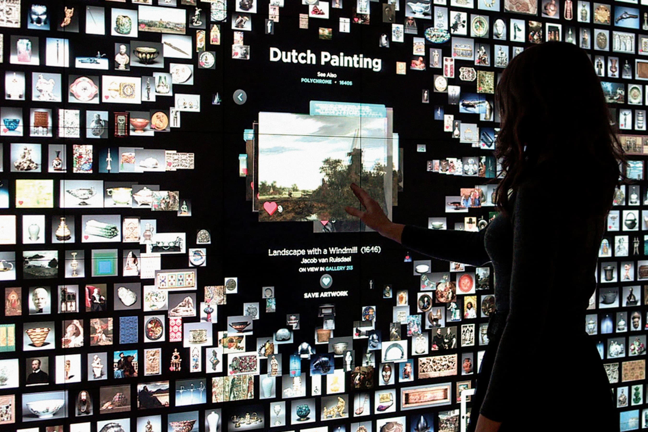 Visitor touches artwork image on large digital display, the image the user is interacting with is larger than dozens of other, smaller artwork thumbnails on the screen.