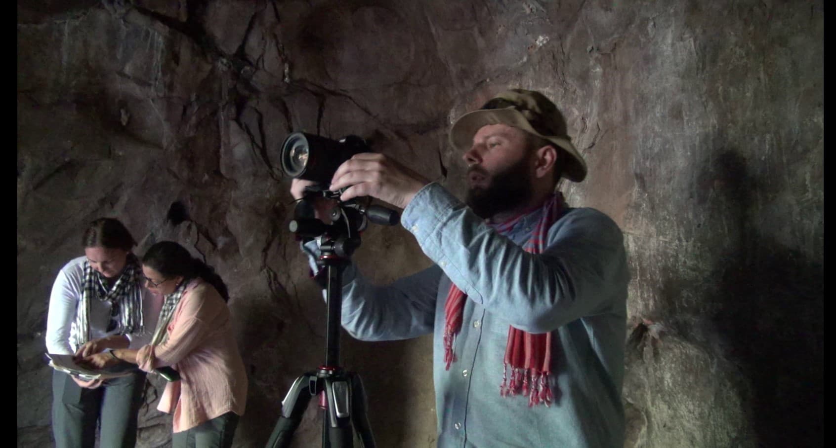 A man looking through a camera in in front of a rocky background