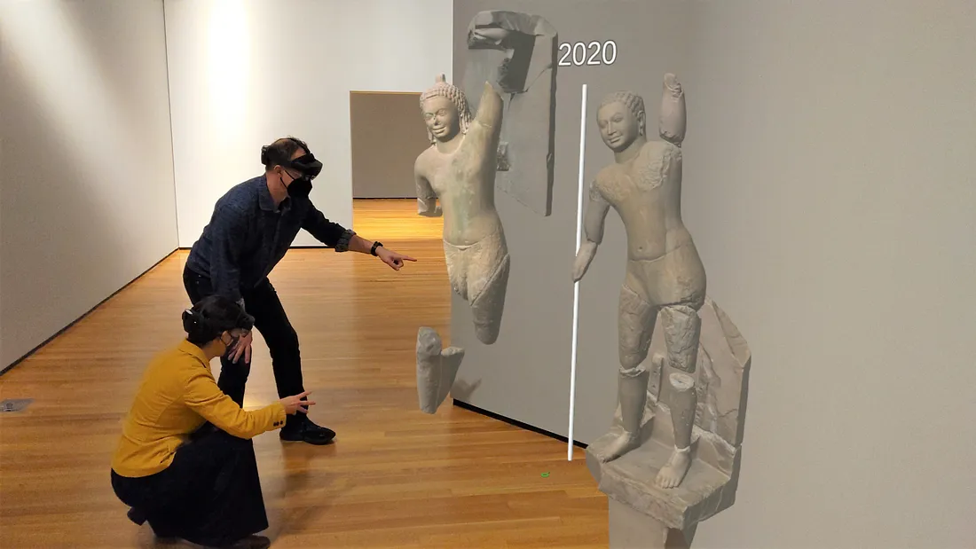 Two figures in a gallery kneeling and pointing at 3-D models of the Cleveland and Phnom Penh sculptures in HoloLens.
