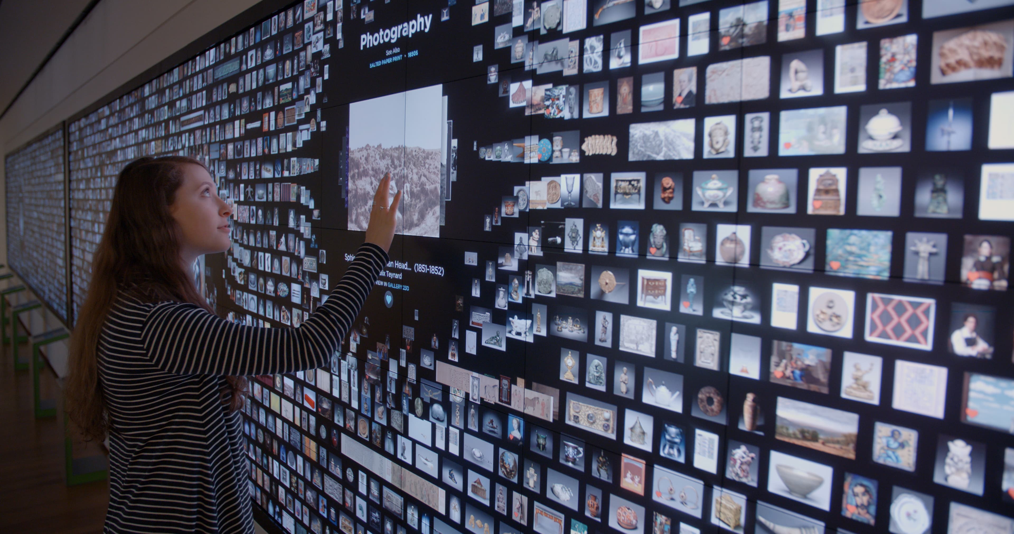 A visitor touching artworks on the collection wall.