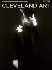 black & white photo of a person in an all black suit, wearing a zebra mask and a white flower in the lapel, tipping a top hat with an all black background by Carrie Mae Weems on the magazine cover