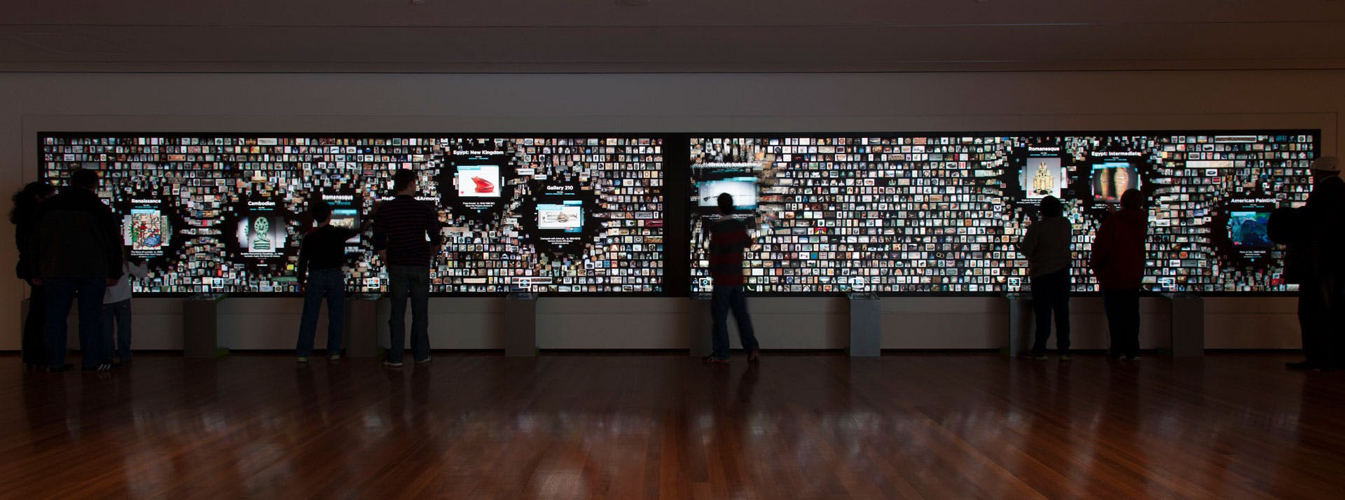 museum visitors exploring a large digital panel with hundreds of images