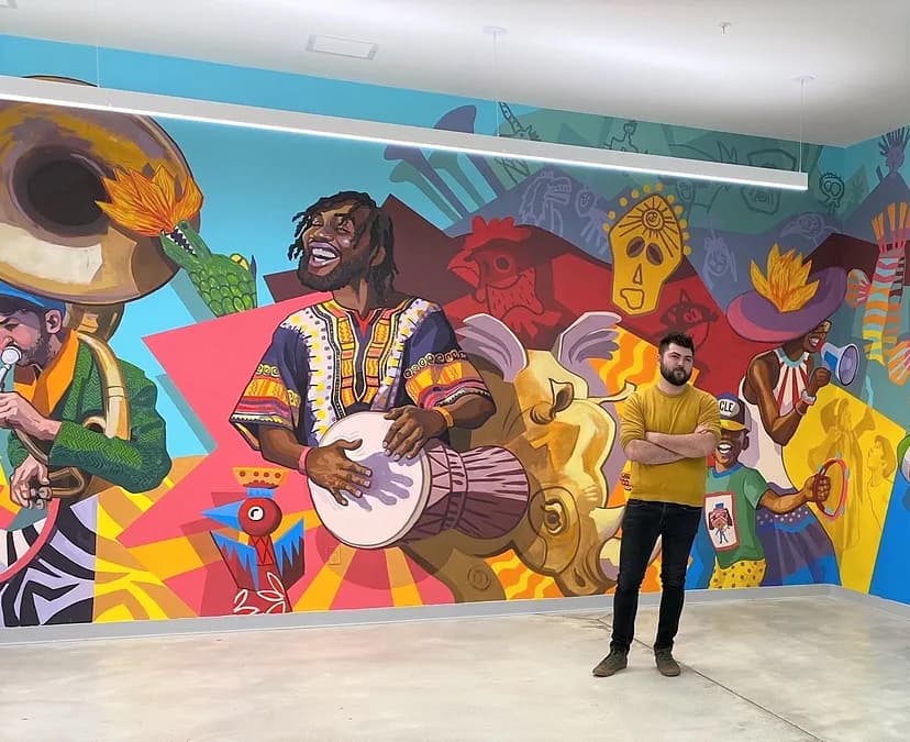 Image of a person standing in front of a vibrantly colored mural with figures playing instruments in front of a backdrop of shapes and animals.