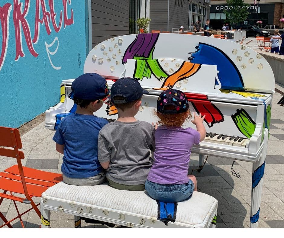Three children seated at a vibrantly painted piano.