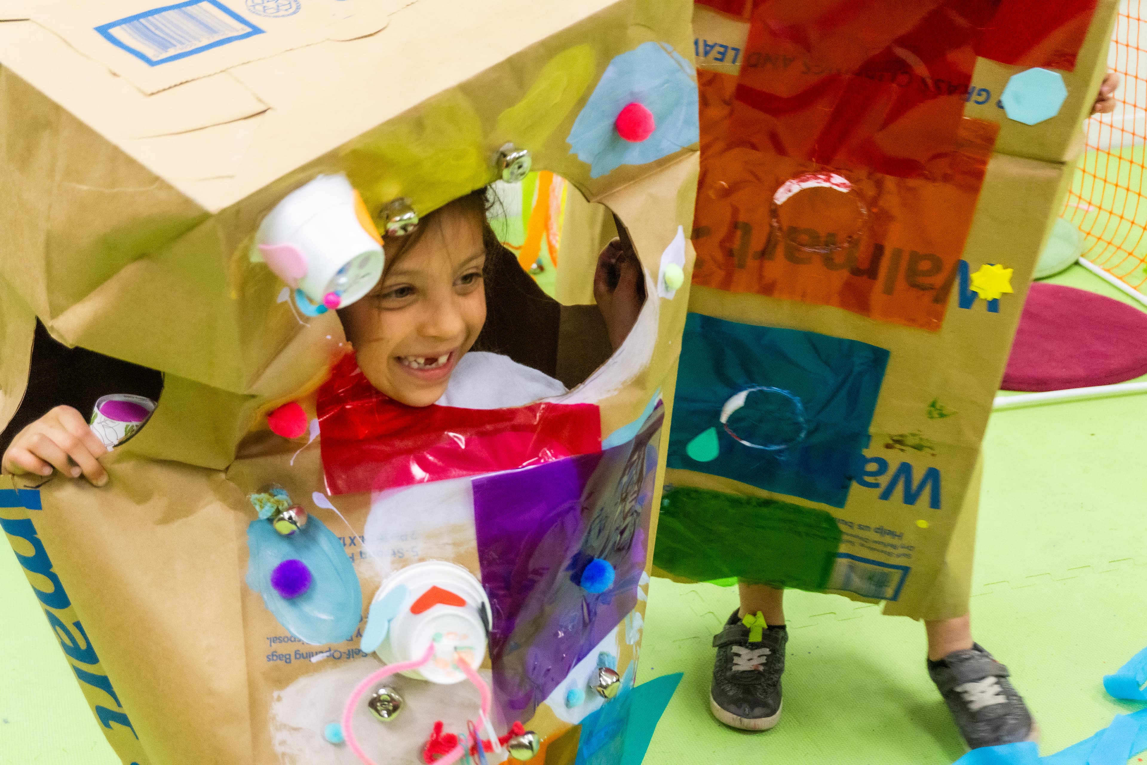 Child inside of brown paper sculpture with objects glued to paper