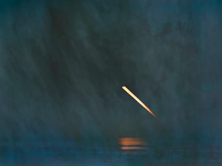 A photo of a streak of moonlight reflecting on water in hazy blue-gray conditions