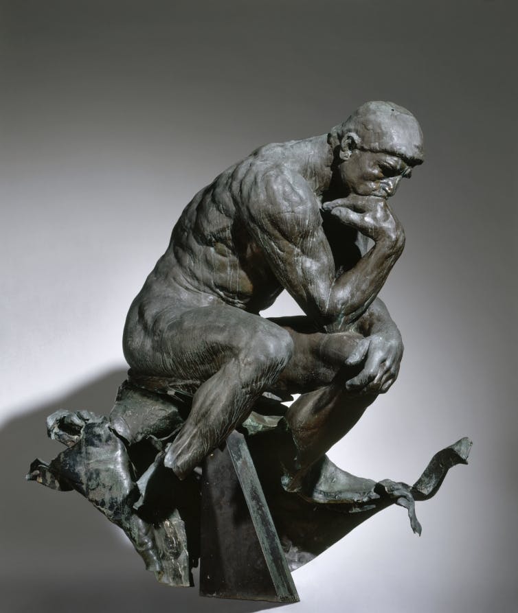 A bronze statue of a man seated, leaning forward with his elbow resting on his knee.