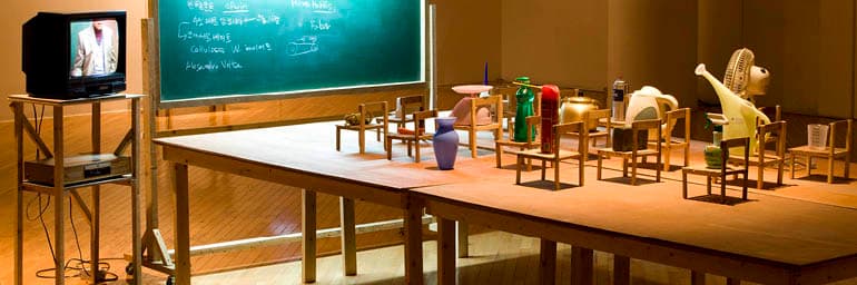 Objects Being Taught They Are Nothing But Tools, 2010. Kim Beom (Korean, b. 1963). Daily objects, wooden chairs, blackboard with fluorescent light, wooden tables, single channel video on TV monitor (21 min., 8 sec.); approx. 165.5 x 427.5 x 230 cm (overall). Courtesy of the artist. © Kim Beom. Photo by Park Myung-Rae
